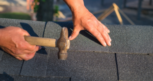 hand holding hammer installing shingles on roof