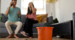 couple sitting on couch on the phone while water is leaking from roof into bucket