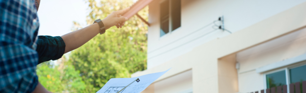 two men looking at roof one pointing other holding paper and measuring tape