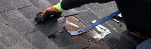 roofer using pry bar to remove damaged shingles