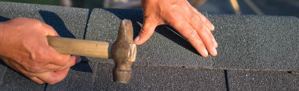 hand holding hammer on shingles