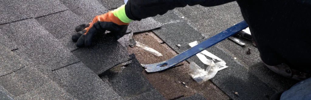 roofer using pry bar to remove damaged shingles